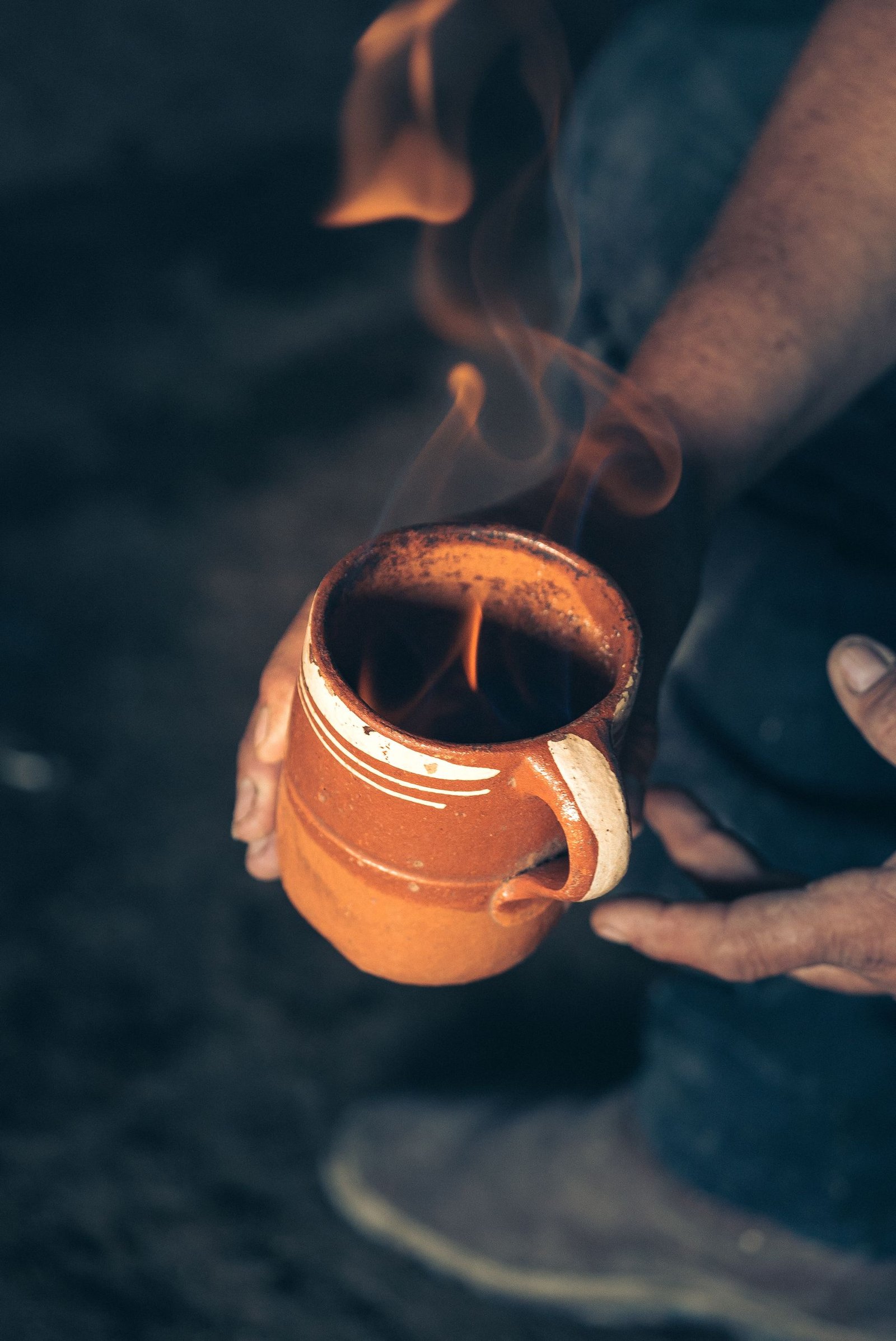 A person holding a ceramic mug with visible flames and smoke rising, creating a dramatic effect.