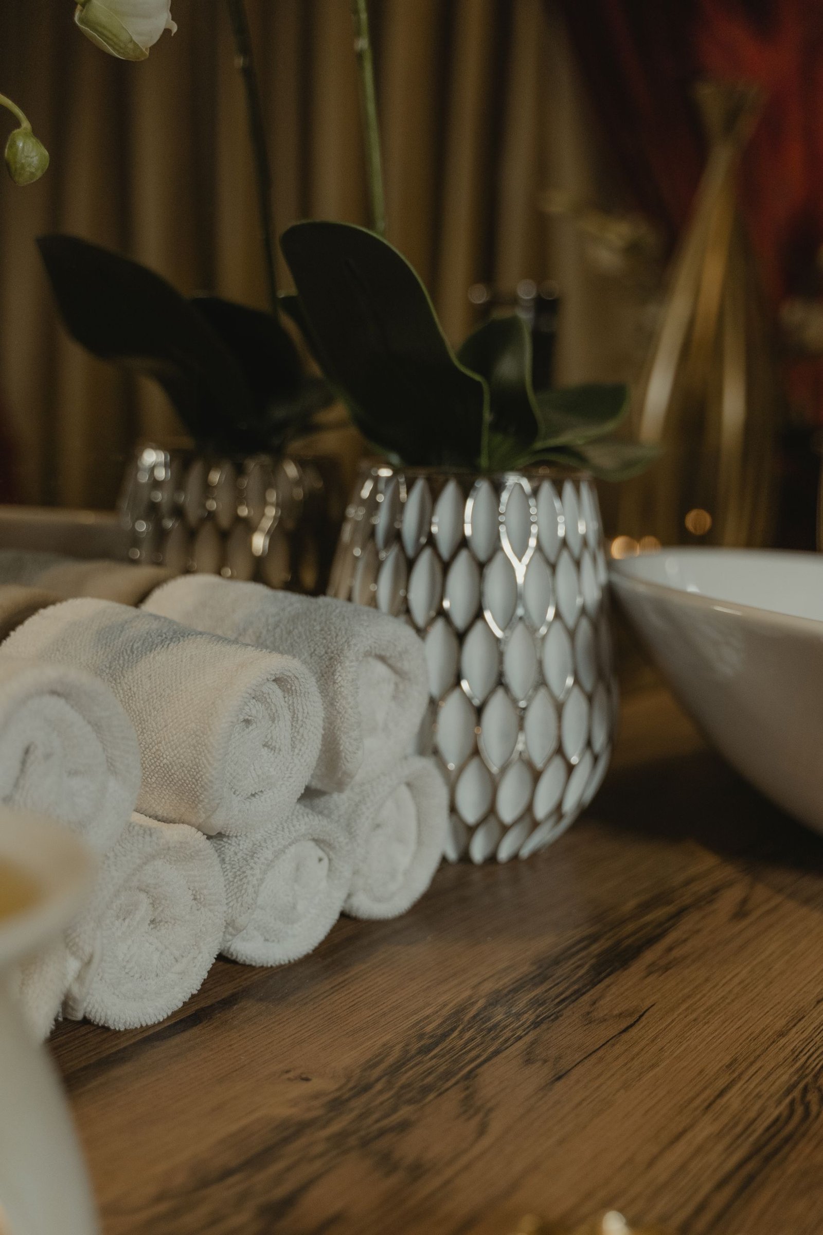A serene spa-like setting featuring rolled towels and a decorative vase on a wooden surface.
